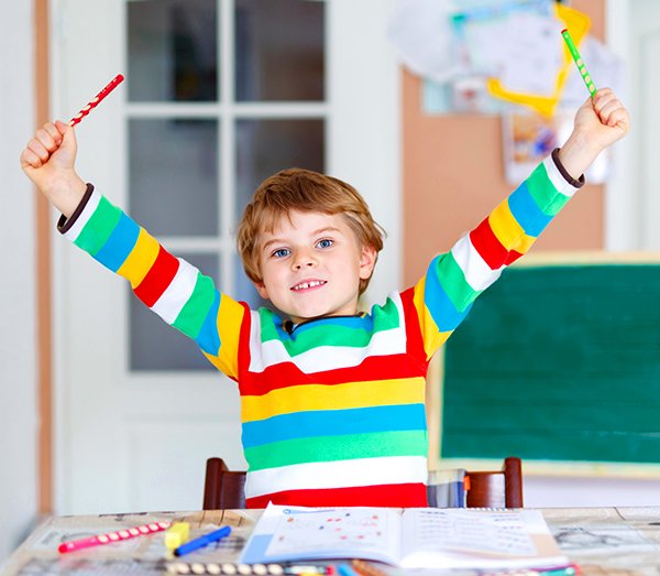 Portrait of cute happy school kid boy at home making homework. Little child writing with colorful pencils, indoors. Elementary school and education